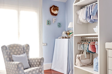 This is an example of a mid-sized beach style nursery for boys in Madrid with blue walls, dark hardwood floors and brown floor.