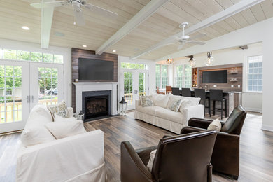 Example of a large country open concept brown floor and medium tone wood floor family room design in Philadelphia with white walls, a standard fireplace, a wood fireplace surround and a wall-mounted tv