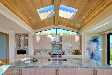 Inspiration for a contemporary galley vaulted ceiling and wood ceiling kitchen remodel in Orange County with an undermount sink, flat-panel cabinets, beige cabinets, green backsplash, stone slab backsplash, stainless steel appliances, an island and turquoise countertops