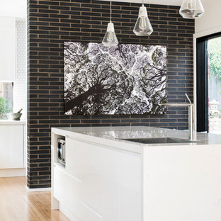 Réalisation d'une grande arrière-cuisine design en L avec un évier posé, un placard à porte plane, des portes de placard blanches, un plan de travail en quartz modifié, une crédence blanche, une crédence en carreau de ciment, un électroménager noir, un sol en bois brun et un îlot central.