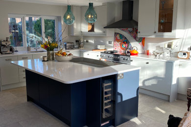 Large contemporary grey and teal l-shaped kitchen/diner in Oxfordshire with an integrated sink, flat-panel cabinets, light wood cabinets, quartz worktops, multi-coloured splashback, glass sheet splashback, stainless steel appliances, porcelain flooring, an island, beige floors, white worktops and feature lighting.
