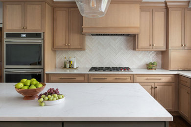 Inspiration for a transitional u-shaped medium tone wood floor and brown floor kitchen remodel in Chicago with a single-bowl sink, flat-panel cabinets, light wood cabinets, quartz countertops, white backsplash, ceramic backsplash, paneled appliances, an island and white countertops