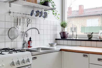 Bild på ett avskilt, mellanstort minimalistiskt l-kök, med en dubbel diskho, släta luckor, vita skåp, träbänkskiva, vitt stänkskydd och vita vitvaror