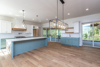 Eat-in kitchen - large transitional l-shaped medium tone wood floor eat-in kitchen idea in Other with a farmhouse sink, recessed-panel cabinets, white cabinets, quartzite countertops, white backsplash, subway tile backsplash, paneled appliances, an island and white countertops