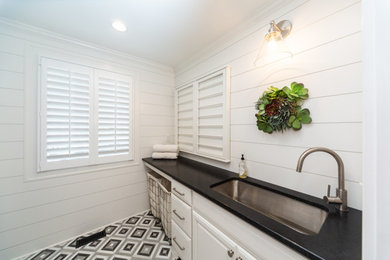 Inspiration for a mid-sized country galley marble floor, gray floor and shiplap wall dedicated laundry room remodel in Charlotte with an undermount sink, raised-panel cabinets, white cabinets, granite countertops, white backsplash, shiplap backsplash, white walls, a stacked washer/dryer and black countertops