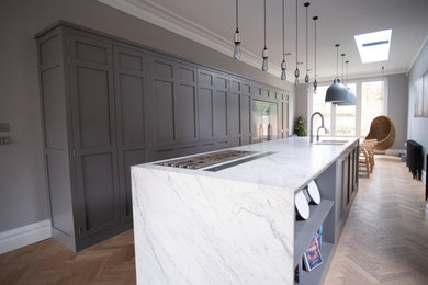Design ideas for a large contemporary grey and white single-wall open plan kitchen in Kent with an integrated sink, shaker cabinets, grey cabinets, marble worktops, stainless steel appliances, an island, brown floors, white worktops, a wallpapered ceiling and feature lighting.