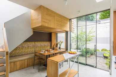 Inspiration for a mid-sized contemporary galley eat-in kitchen in London with a drop-in sink, flat-panel cabinets, white cabinets, solid surface benchtops, brown splashback, timber splashback, concrete floors, with island, grey floor and white benchtop.