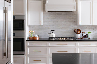 Mid-sized transitional l-shaped dark wood floor and brown floor open concept kitchen photo in Austin with an undermount sink, shaker cabinets, white cabinets, soapstone countertops, white backsplash, stainless steel appliances, an island and black countertops
