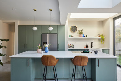 This is an example of a medium sized contemporary single-wall kitchen/diner in London with recessed-panel cabinets, white splashback, engineered quartz splashback, an island and white worktops.