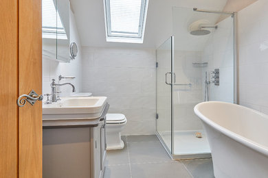 Large classic family bathroom in Surrey with shaker cabinets, grey cabinets, a freestanding bath, a corner shower, a one-piece toilet, white tiles, porcelain tiles, white walls, porcelain flooring, a console sink, granite worktops, grey floors, a hinged door and black worktops.