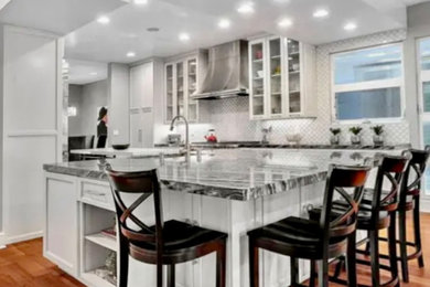 Example of a large transitional galley dark wood floor kitchen design in Los Angeles with glass-front cabinets, white cabinets, stainless steel appliances, an island and black countertops
