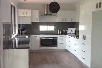 Photo of a modern kitchen in Sunshine Coast with white cabinets, a drop-in sink, flat-panel cabinets, laminate benchtops, grey splashback, ceramic splashback, stainless steel appliances and vinyl floors.