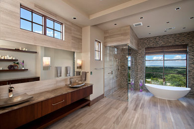 Photo of a large contemporary master bathroom in Austin with a vessel sink, flat-panel cabinets, dark wood cabinets, a freestanding tub, a corner shower, beige tile, marble benchtops, stone tile, beige walls and light hardwood floors.