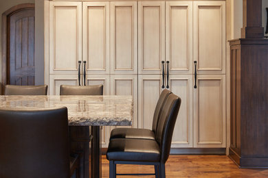 Large transitional u-shaped medium tone wood floor and brown floor eat-in kitchen photo in Omaha with a farmhouse sink, shaker cabinets, distressed cabinets, granite countertops, white backsplash, glass tile backsplash, paneled appliances and an island