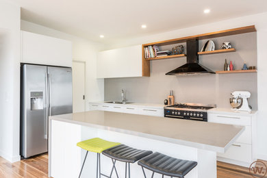 This is an example of a mid-sized galley kitchen pantry in Melbourne with a farmhouse sink, flat-panel cabinets, yellow cabinets, glass benchtops, grey splashback, porcelain splashback, black appliances, limestone floors and with island.
