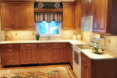 Inspiration for a mid-sized transitional medium tone wood floor eat-in kitchen remodel in New York with raised-panel cabinets, medium tone wood cabinets, solid surface countertops, ceramic backsplash, white appliances, no island, an undermount sink and beige backsplash