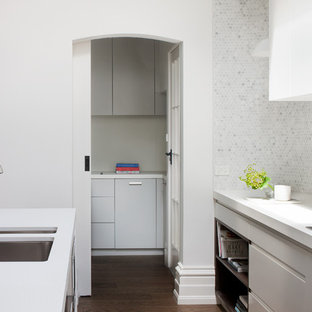 Cette image montre une grande arrière-cuisine linéaire design avec un évier 2 bacs, un placard à porte affleurante, des portes de placard blanches, un plan de travail en stratifié, une crédence en dalle de pierre, un électroménager en acier inoxydable et un îlot central.