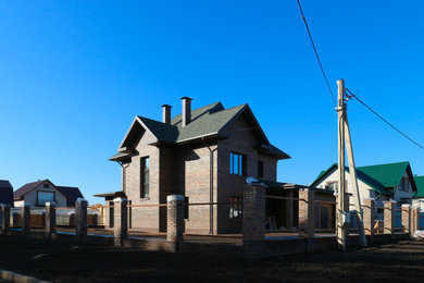 На фото: двухэтажный, кирпичный, коричневый частный загородный дом среднего размера с вальмовой крышей, крышей из гибкой черепицы и синей крышей