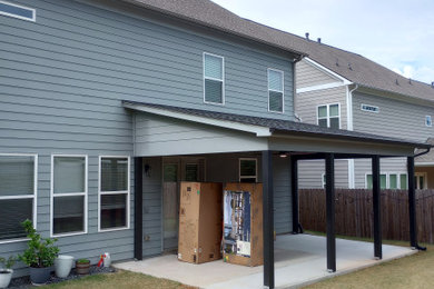 Large trendy concrete wood railing back porch photo in Other with a roof extension