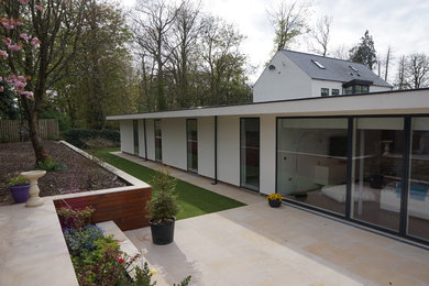 Exempel på ett stort modernt vitt hus, med allt i ett plan, platt tak, tak i mixade material och stuckatur