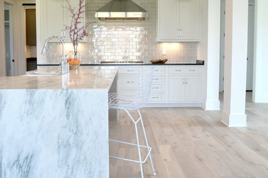 Inspiration for a large cottage l-shaped medium tone wood floor and beige floor kitchen remodel in Indianapolis with recessed-panel cabinets, white cabinets, marble countertops, gray backsplash, subway tile backsplash, stainless steel appliances, an island, a farmhouse sink and white countertops