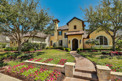 Large southwestern yellow two-story stucco house exterior idea in Houston with a tile roof and a brown roof