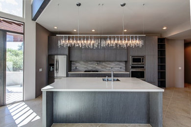 Example of a mid-sized southwest galley ceramic tile and beige floor open concept kitchen design in Phoenix with an undermount sink, flat-panel cabinets, gray cabinets, quartzite countertops, gray backsplash, ceramic backsplash, stainless steel appliances and an island