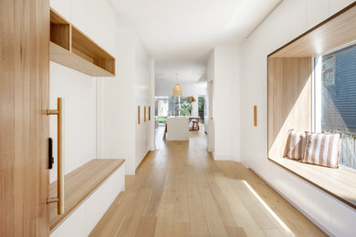 This is an example of a mid-sized beach style mudroom in Sydney with white walls, light hardwood floors, a single front door and a light wood front door.