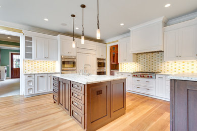 This is an example of a large arts and crafts u-shaped separate kitchen in DC Metro with a farmhouse sink, recessed-panel cabinets, white cabinets, granite benchtops, multi-coloured splashback, ceramic splashback, panelled appliances, medium hardwood floors, with island, brown floor and white benchtop.