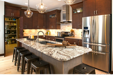 Mid-sized elegant l-shaped light wood floor enclosed kitchen photo in Salt Lake City with a double-bowl sink, flat-panel cabinets, brown cabinets, quartzite countertops, beige backsplash, stone tile backsplash, stainless steel appliances and an island