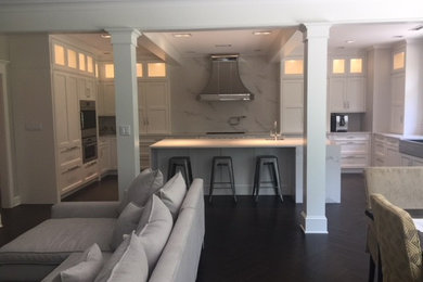 Large transitional u-shaped vinyl floor and black floor open concept kitchen photo in Other with a farmhouse sink, recessed-panel cabinets, white cabinets, white backsplash, paneled appliances, an island, white countertops, quartz countertops and quartz backsplash