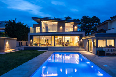 Large contemporary back rectangular lengths swimming pool in Dorset with with pool landscaping and natural stone paving.