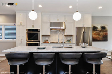 Mid-sized trendy single-wall light wood floor open concept kitchen photo in Chicago with marble countertops, an undermount sink, shaker cabinets, white cabinets, white backsplash, ceramic backsplash, stainless steel appliances and an island
