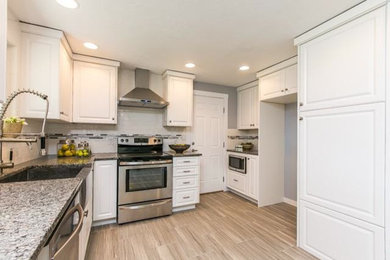 Example of a classic u-shaped medium tone wood floor and beige floor eat-in kitchen design in Boise with an undermount sink, raised-panel cabinets, white cabinets, granite countertops, white backsplash, subway tile backsplash, stainless steel appliances and a peninsula