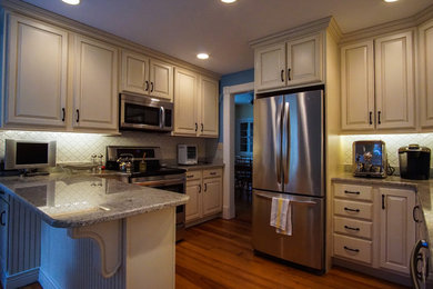 Example of a mid-sized transitional l-shaped medium tone wood floor and brown floor enclosed kitchen design in New York with an undermount sink, white cabinets, granite countertops, white backsplash, stainless steel appliances, a peninsula, raised-panel cabinets and multicolored countertops