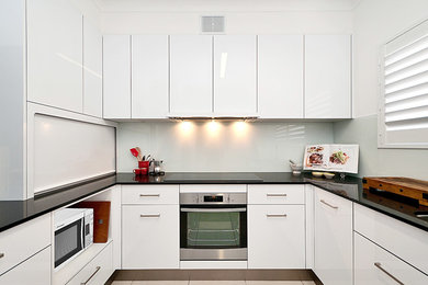 Photo of a mid-sized contemporary u-shaped separate kitchen in Gold Coast - Tweed with flat-panel cabinets, white cabinets, quartz benchtops, white splashback, glass sheet splashback, stainless steel appliances, no island, an undermount sink and ceramic floors.