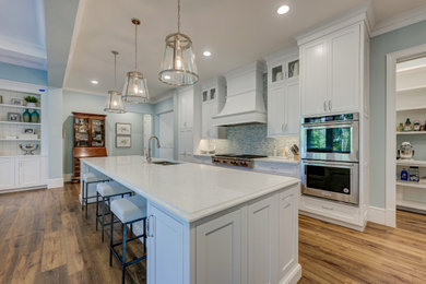 Example of a mid-sized beach style l-shaped medium tone wood floor and brown floor eat-in kitchen design in Other with an undermount sink, shaker cabinets, white cabinets, marble countertops, blue backsplash, glass tile backsplash, stainless steel appliances, an island and white countertops