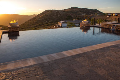 This is an example of a large mediterranean backyard rectangular infinity pool in San Diego with concrete pavers.