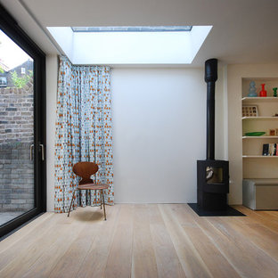 Photo of a medium sized contemporary basement in London with white walls, light hardwood flooring and a wood burning stove.
