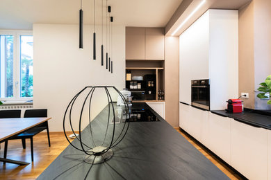 This is an example of a large modern l-shaped eat-in kitchen in Other with beaded inset cabinets, white cabinets, a peninsula, a drop-in sink, black appliances, medium hardwood floors, brown floor, black benchtop and recessed.