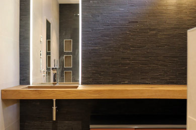 Réalisation d'une salle de bain design de taille moyenne avec un placard à porte affleurante, des portes de placard violettes, WC suspendus, un carrelage noir, du carrelage en ardoise, un mur beige, un sol en carrelage de céramique, un lavabo suspendu, un plan de toilette en verre, un sol beige, une cabine de douche à porte battante et un plan de toilette marron.