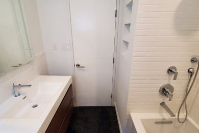 ロサンゼルスにある広いモダンスタイルのおしゃれなマスターバスルーム (フラットパネル扉のキャビネット、濃色木目調キャビネット、アルコーブ型浴槽、シャワー付き浴槽	、白いタイル、サブウェイタイル、白い洗面カウンター、洗面台1つ、フローティング洗面台、一体型シンク、分離型トイレ、白い壁、セラミックタイルの床、黒い床) の写真