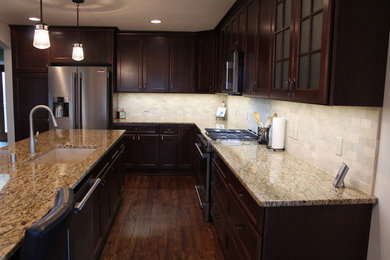 Example of a mid-sized classic u-shaped dark wood floor and brown floor enclosed kitchen design in Milwaukee with an undermount sink, recessed-panel cabinets, dark wood cabinets, granite countertops, white backsplash, stone tile backsplash, stainless steel appliances and an island
