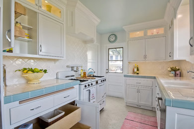 Inspiration for a mid-sized transitional galley separate kitchen in San Diego with a double-bowl sink, recessed-panel cabinets, white cabinets, tile benchtops, white splashback, ceramic splashback, white appliances, terrazzo floors and no island.