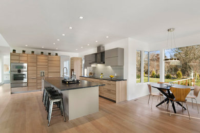 Example of a trendy l-shaped medium tone wood floor and brown floor kitchen design in New York with flat-panel cabinets, light wood cabinets, stainless steel appliances and an island