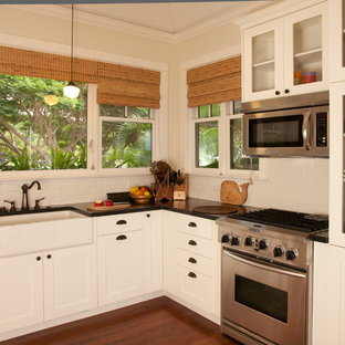 Inspiration for a mid-sized tropical u-shaped kitchen pantry in Hawaii with a farmhouse sink, flat-panel cabinets, white cabinets, solid surface benchtops, white splashback, ceramic splashback, stainless steel appliances, dark hardwood floors and no island.