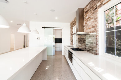 Photo of a large traditional galley open plan kitchen in Brisbane with a double-bowl sink, white cabinets, multi-coloured splashback, brick splashback, black appliances, with island, multi-coloured floor, quartz benchtops, ceramic floors and white benchtop.