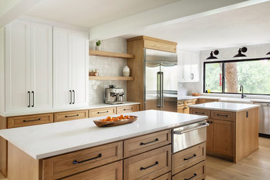 Inspiration for a mid-sized country u-shaped light wood floor kitchen pantry remodel in Dallas with a farmhouse sink, shaker cabinets, brown cabinets, quartz countertops, white backsplash, ceramic backsplash, stainless steel appliances, two islands and white countertops