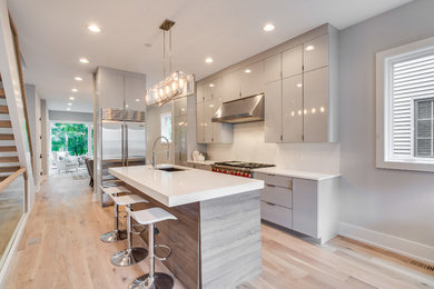 This is an example of a mid-sized contemporary single-wall open plan kitchen in Chicago with with island, an undermount sink, flat-panel cabinets, yellow cabinets, quartz benchtops, white splashback, subway tile splashback, stainless steel appliances and light hardwood floors.