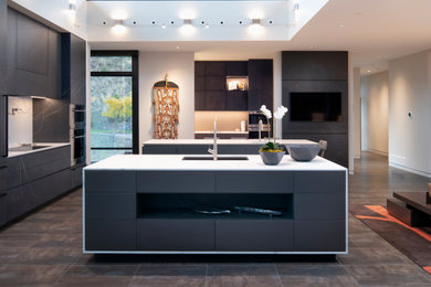 Example of a trendy brown floor and vaulted ceiling kitchen design in Other with an undermount sink, flat-panel cabinets, gray cabinets, white backsplash, stone slab backsplash, stainless steel appliances, an island and white countertops